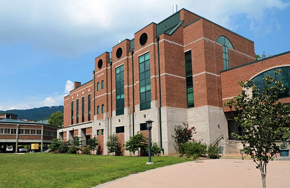 A modern brick university building with large windows and landscaped surroundings.